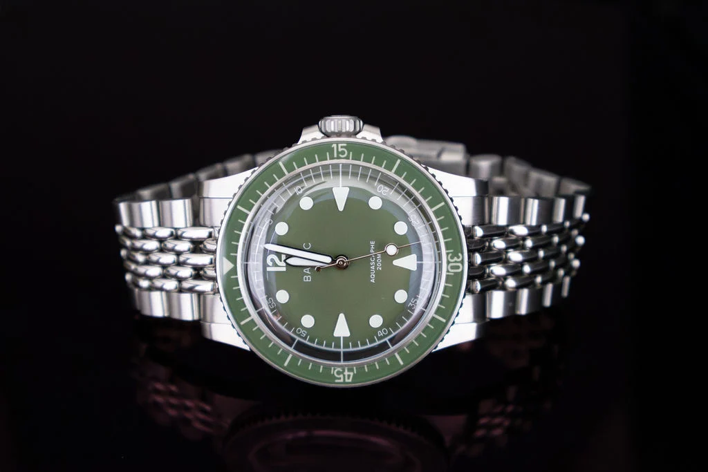 Reloj de acero con carátula verde sobre fondo oscuro